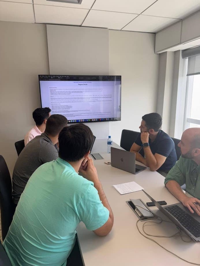 Reunião de trabalho em volta da mesa, com o time analisando um documento na tela