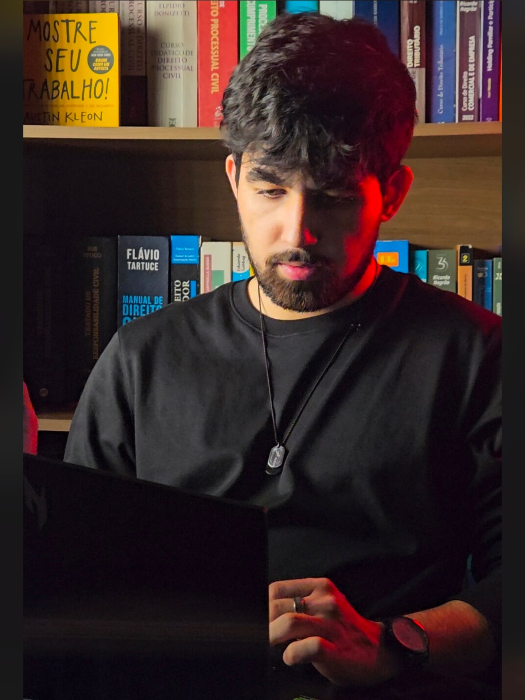 Felipe trabalhando no notebook, sentado em frente a uma estante de livros